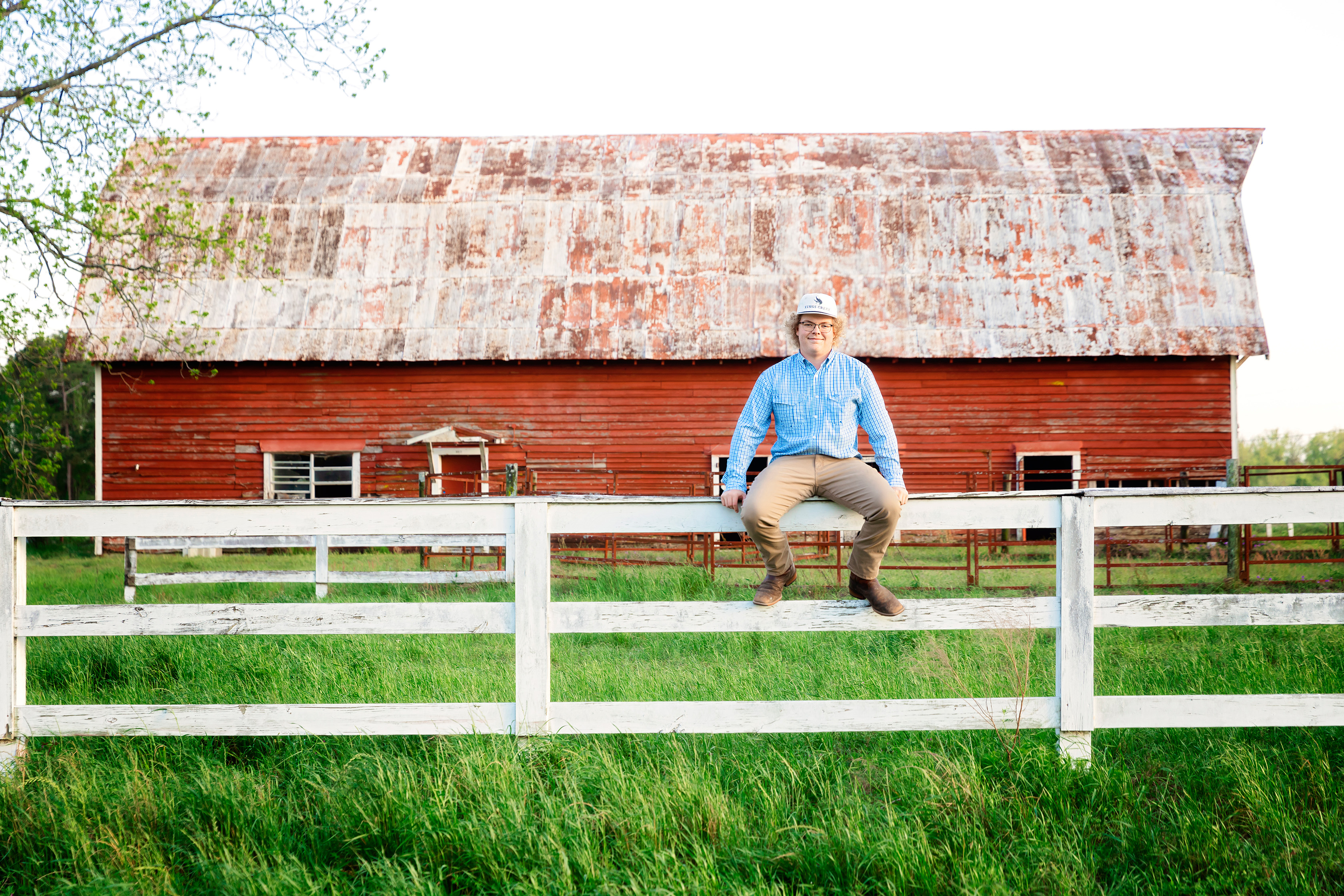 Man sits on fence with a barn in the background
