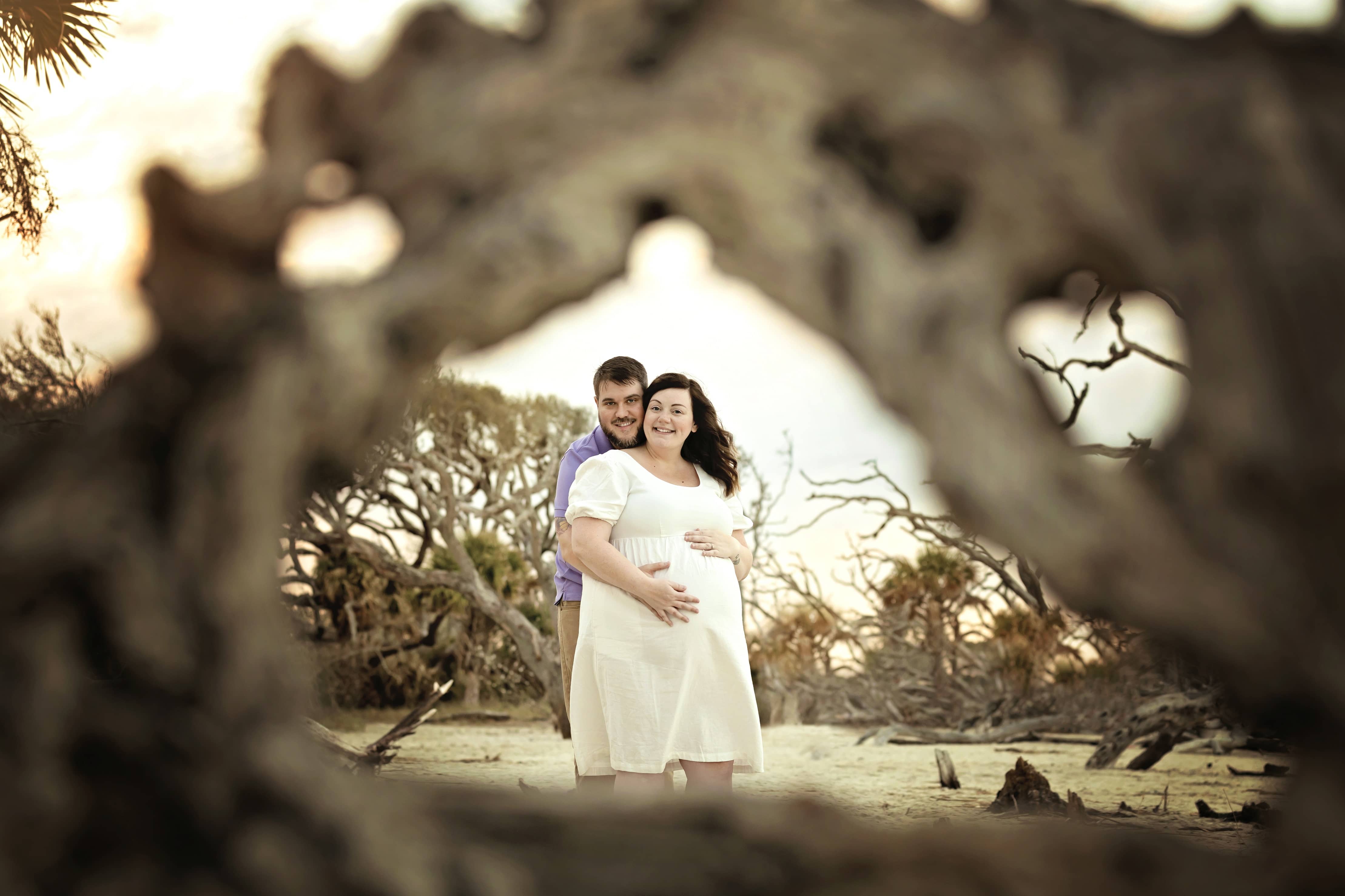 Couple holds each other next to driftwood on the beach