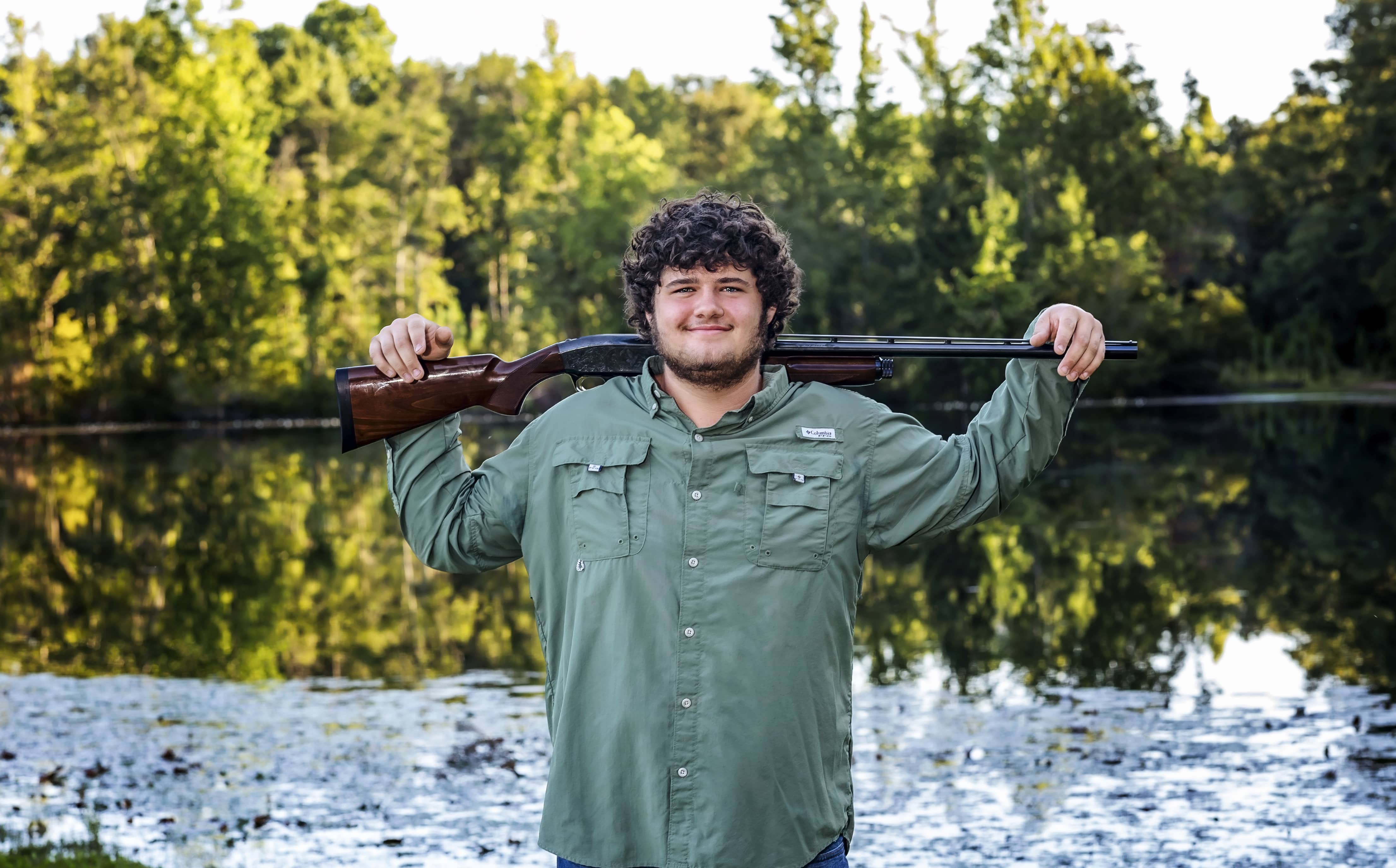 Man poses with his hunting weapon with a lake in the background